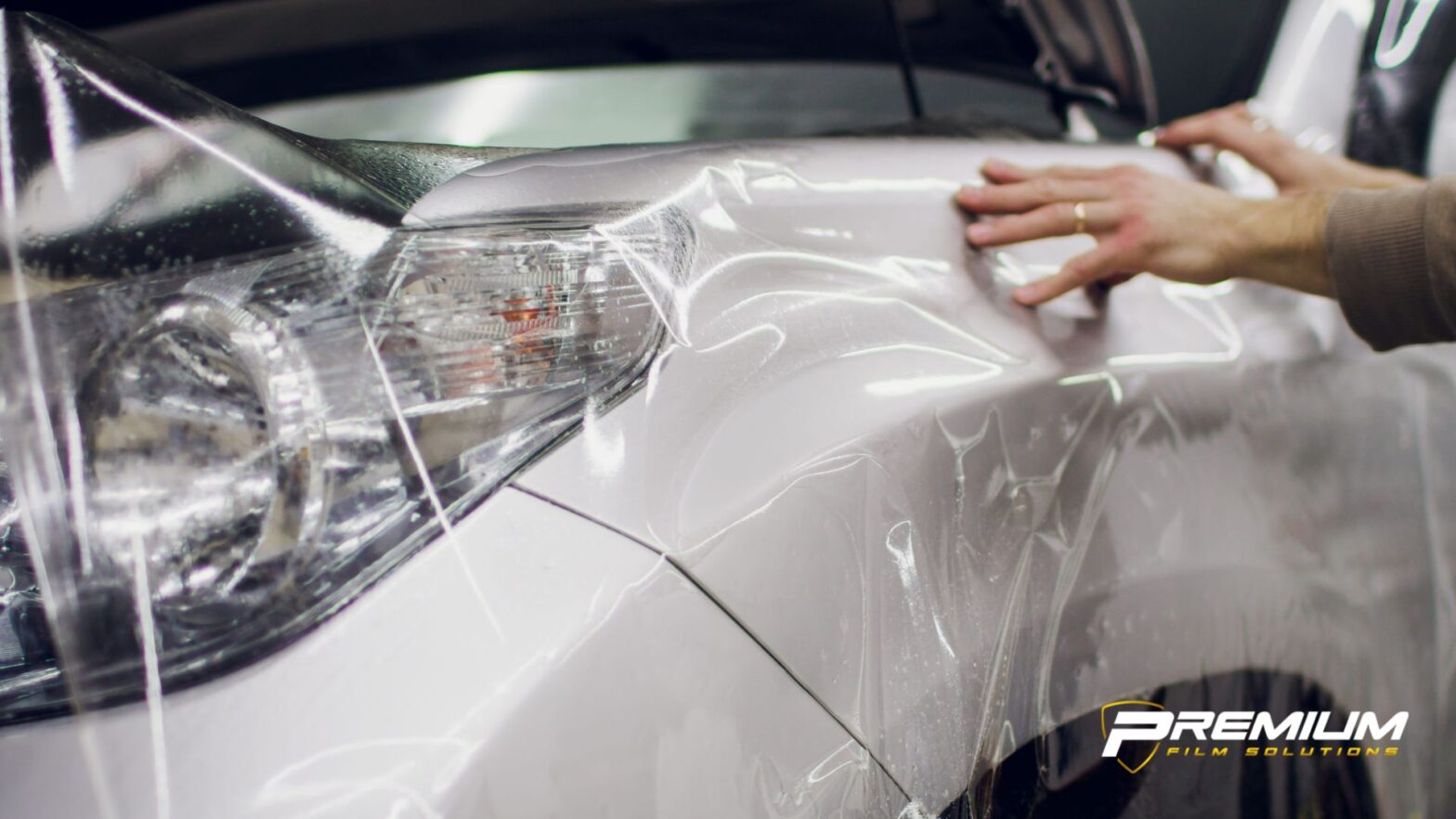 Installer stretching and pressing transparent paint protection film onto a white car bumper for seamless coverage and impact protection.