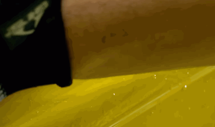 Close up of a glossy yellow car panel with water droplets beading on the surface after paint protection film application.