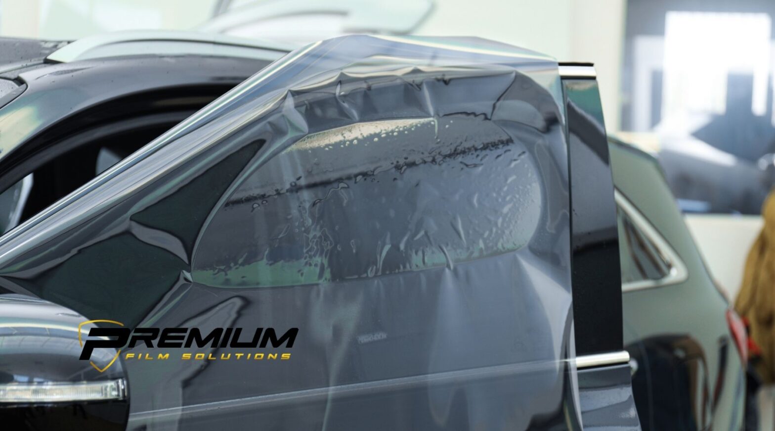 Premium Film Solutions applying automotive window tint film to a vehicle side window.