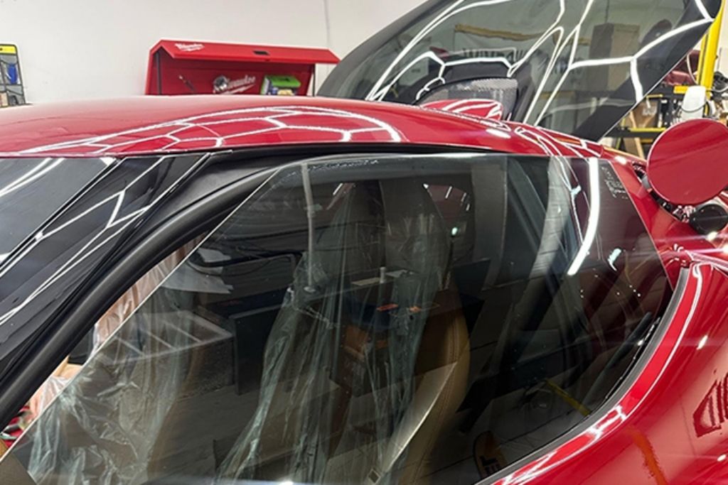 Red sports car with professionally tinted side window inside an automotive film installation shop.