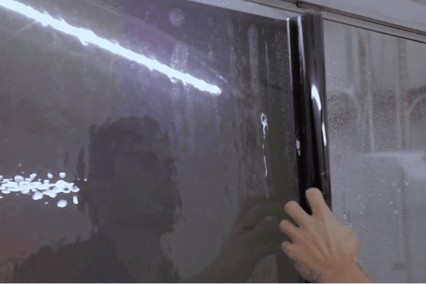 Installer smoothing window tint film onto glass during a professional film application.